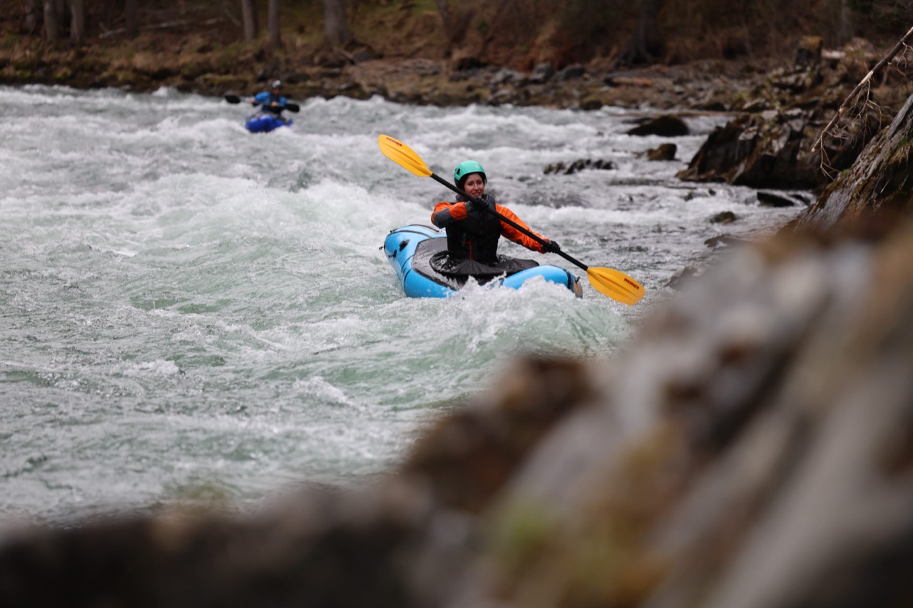 Mona paddling a blue packraft through whitewater with a yellow paddle